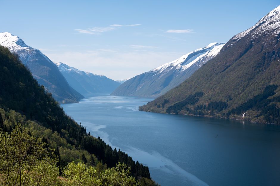 Breathtaking view of Sogndalsfjøra fjord with snow-capped mountains and lush green forests.