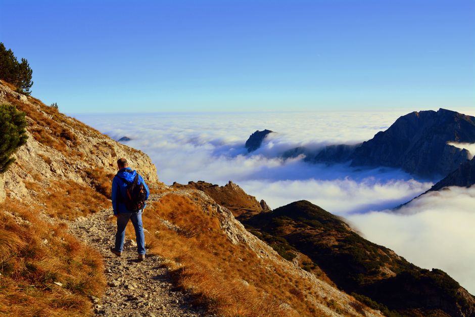 A hiker in a blue jacket enjoying the breathtaking mountain view above the clouds on a clear day.