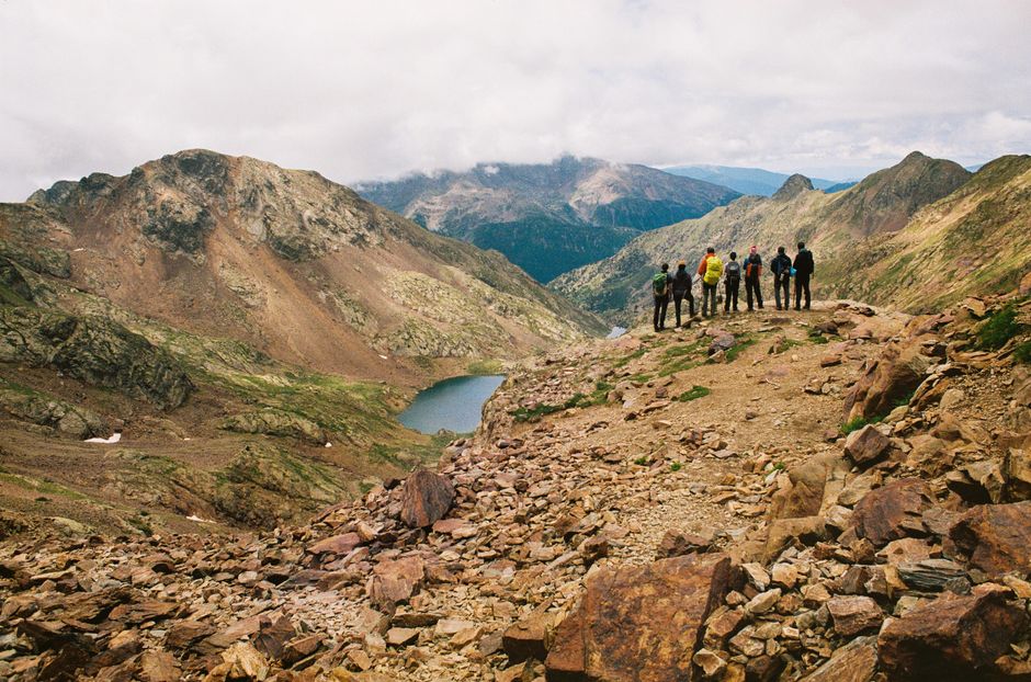 Group of hikers atop a mountain overlooking a scenic valley with a lake in the distance.